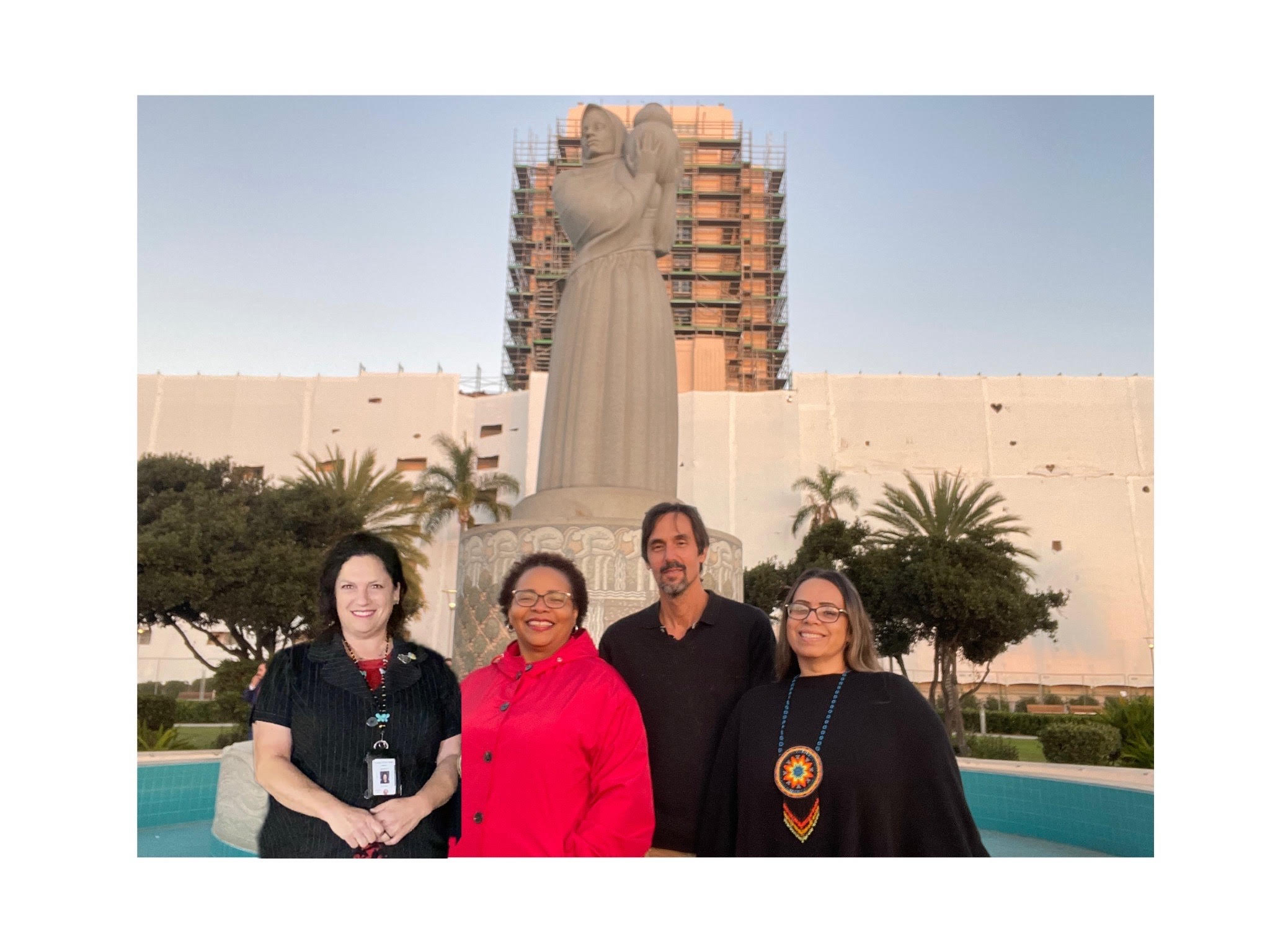 Maria Whitehorse se tient aux côtés de trois autres militants devant une statue géante d'une femme tenant une olla devant le bâtiment administratif du comté de San Diego.  Crédit : Maria Whitehorse.