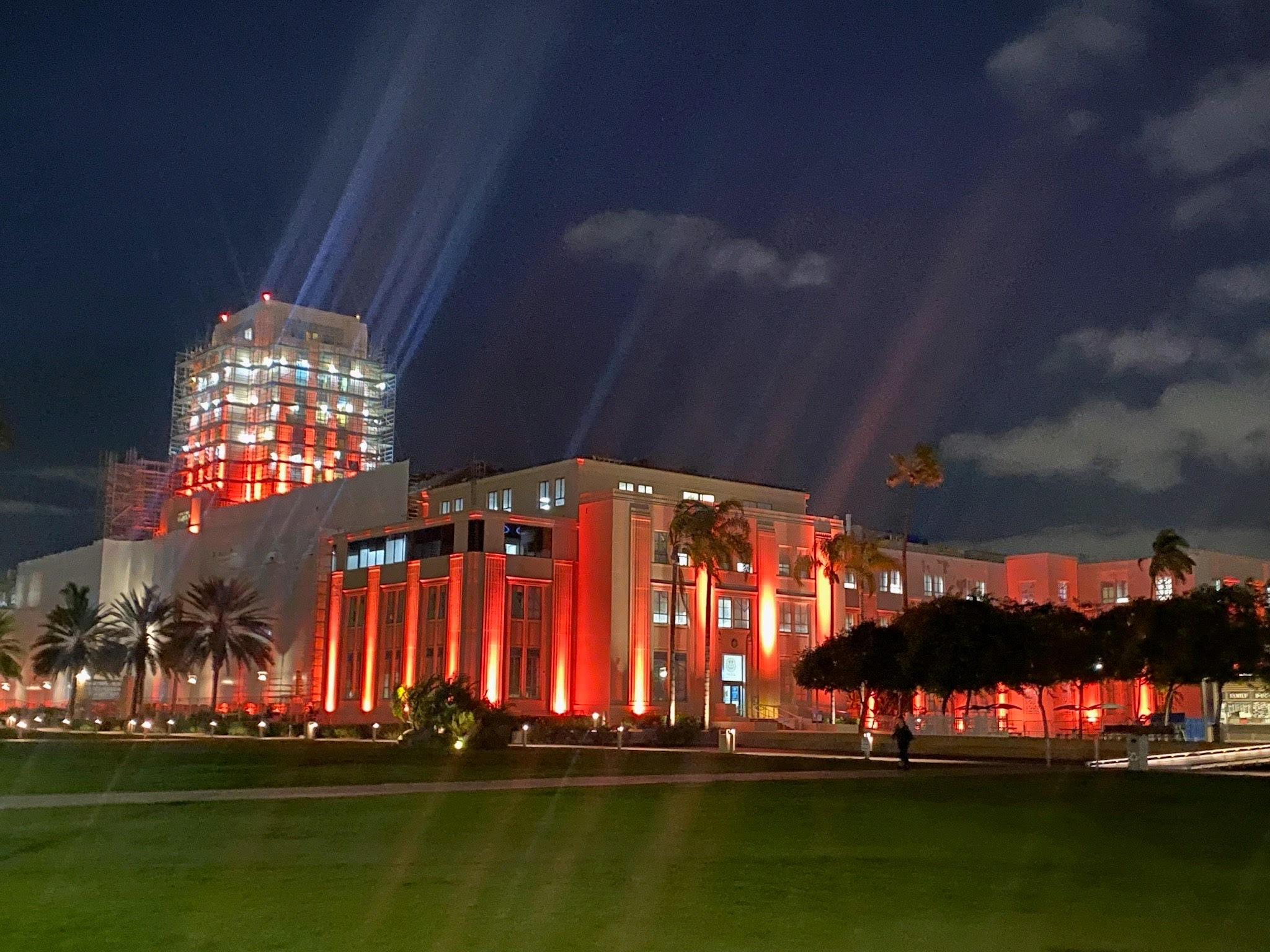 Le bâtiment administratif du comté de San Diego, un grand bâtiment rectangulaire, est représenté sous un ciel nocturne partiellement nuageux et est éclairé par des néons orange vif sur la façade du bâtiment.